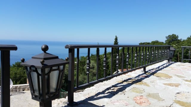 View from the villa terrace in Šušanj, Montenegro: stone floor, wrought-iron railings, a street lamp, and panoramic sea views.