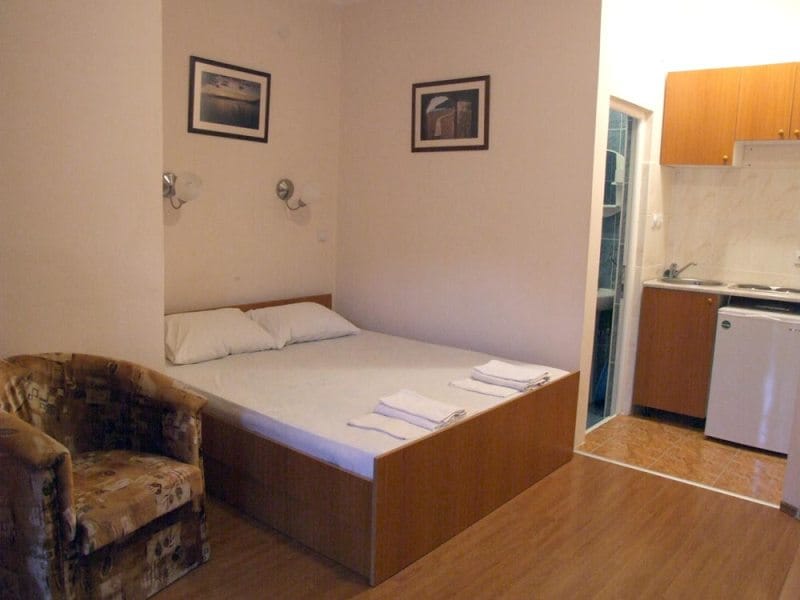 Spavaća soba u apartmanu u Bečićima, Crna Gora: bračni krevet, fotelja i ugrađena mini-kuhinja sa uređajima.