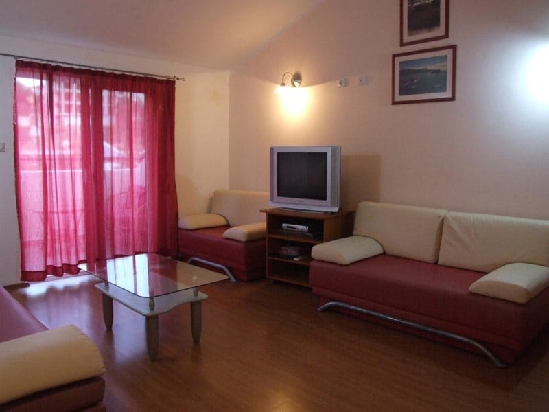Dnevna soba u kući u Bečićima, Crna Gora: mekani nameštaj, stakleni stočić, TV zona i izlaz na balkon.