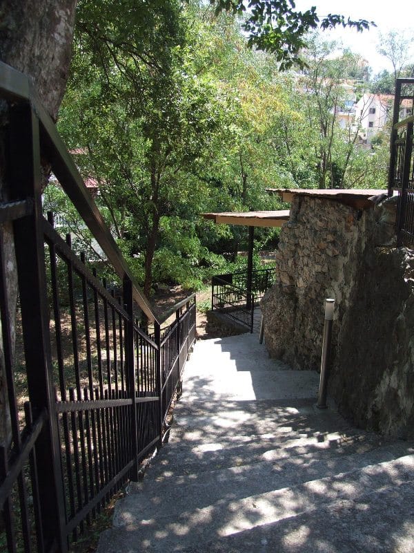 Kameno stepenište sa kovanim ogradama u zelenoj bašti kuće u Bečićima, Crna Gora, koje vodi do stambenog placa.