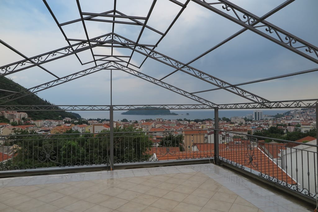 Terasa sa kovanim nadstrešnicom i panoramskim pogledom na more i grad Budvu, Crna Gora. Popločan pod, metalna ograda.