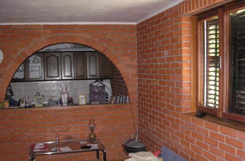 Dnevna soba sa zidom od cigle i lučnim prolazom ka kuhinji u kući, Bečići, Crna Gora.