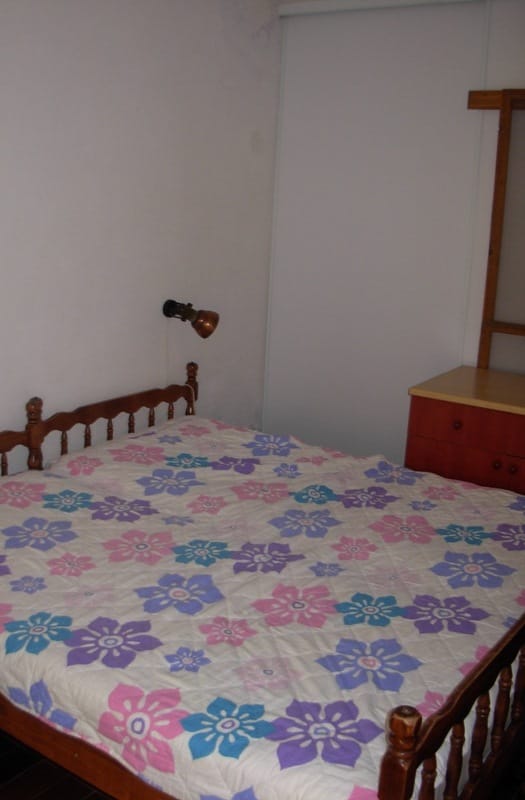 Spavaća soba sa drvenim krevetom i komodom u kući na prodaju u Bečićima, Crna Gora. Udoban enterijer sa cvetnim prekrivačem.