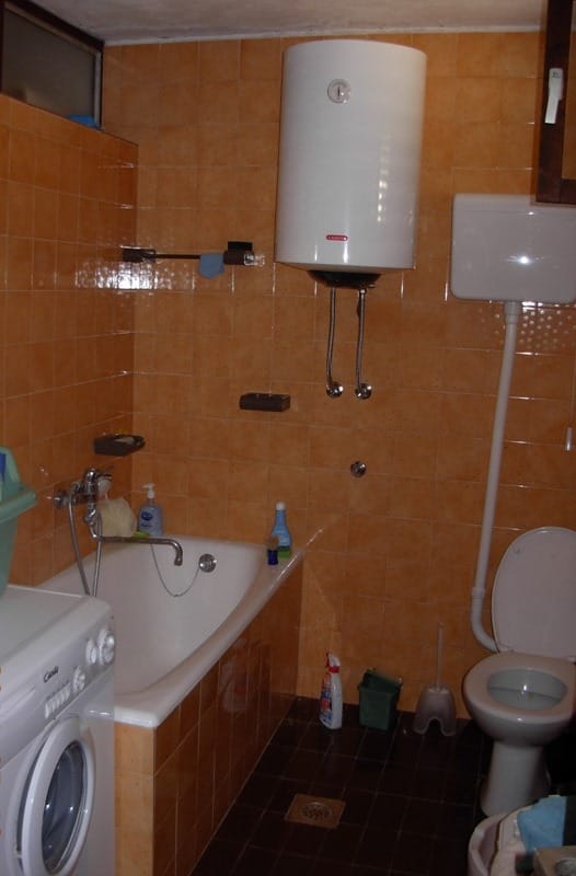 Kupatilo u kući u Bečićima, Crna Gora: narandžaste pločice, kada, bojler i veš mašina.