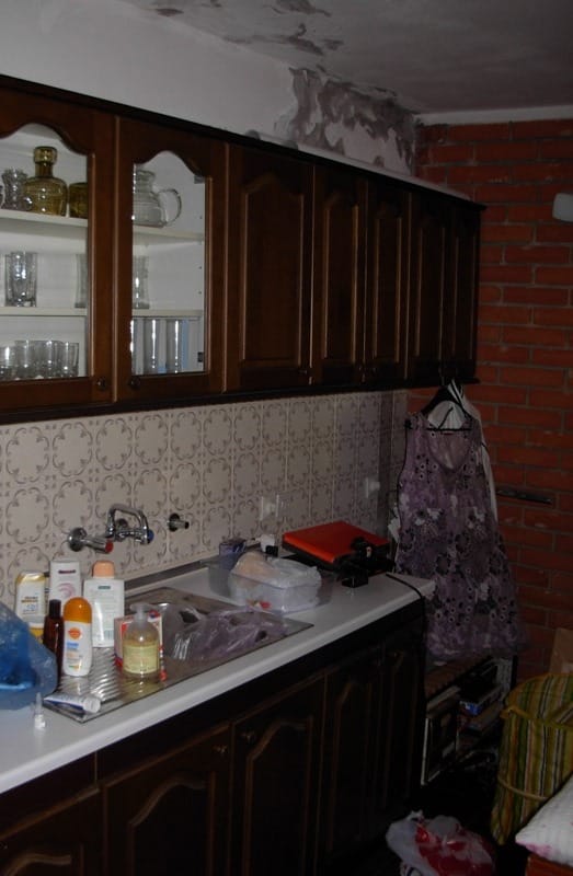 Kuhinja u kući u Bečićima, Crna Gora: tamni drveni kuhinjski elementi, dekorativni zidni panel s uzorkom i akcentni zid od crvene cigle.