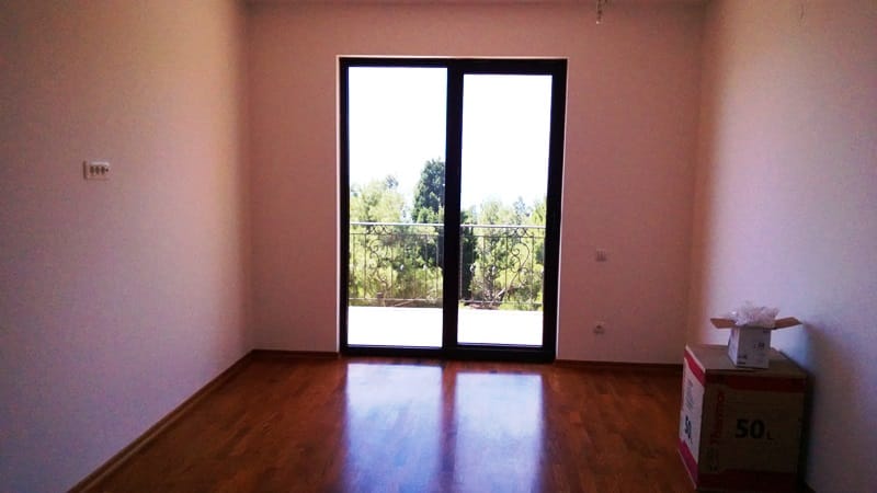 Svetla dnevna soba sa parketnim podom i izlazom na balkon u kući, Šušanj, Crna Gora, pogled na zelenilo i borove.