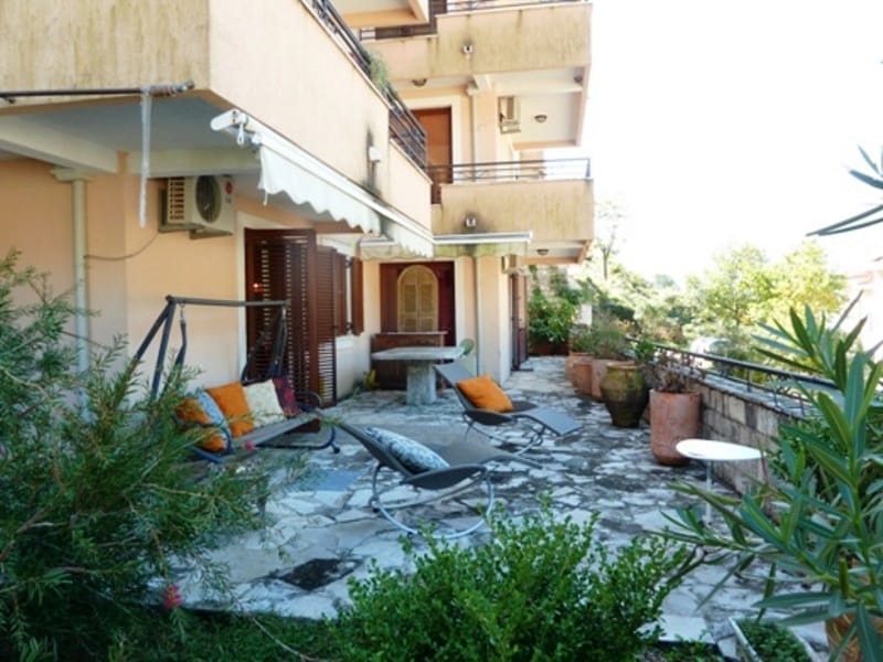 Spacious terrace with garden furniture and a swing in an apartment in Risan, Montenegro, overlooking a green garden.