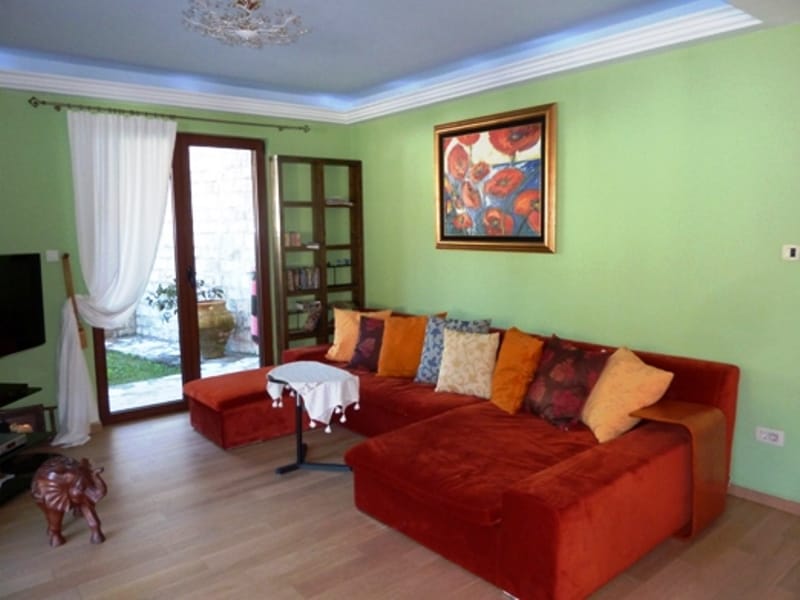 Living room in an apartment in Risan, Montenegro: bright red sofa, green walls, access to the terrace, and parquet flooring.