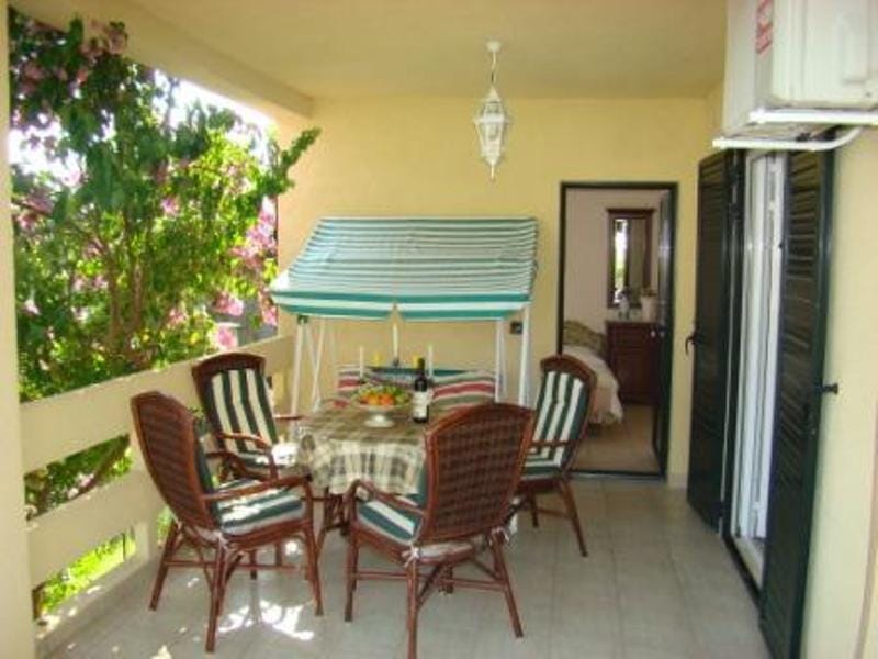 Cozy terrace with wicker furniture and a swing at a villa in Shushan, Montenegro, overlooking a blooming garden and a room.