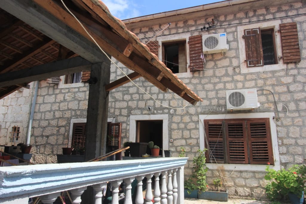 Façade d’une maison traditionnelle en pierre avec volets en bois et terrasse à Dobrota, Monténégro.