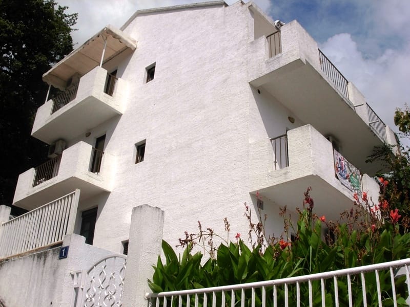 Trospratna bela kuća sa balkonima i terasama u gradu Petrovac, Crna Gora, pogled na fasadu zgrade sa ulice.