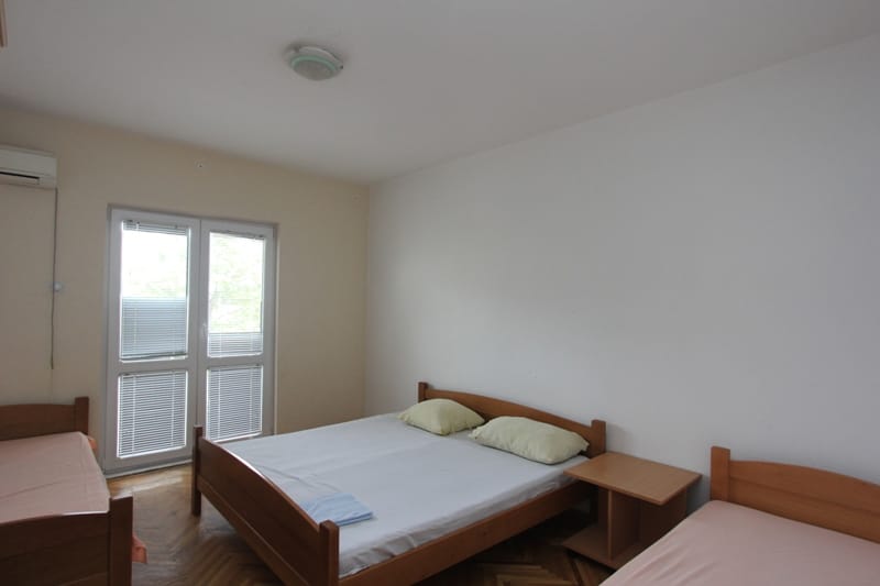 Svetla spavaća soba sa tri drvena kreveta i izlazom na balkon u kući, Sutomore, Crna Gora.