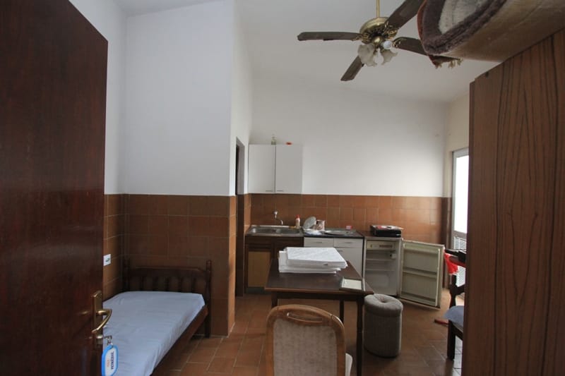 Kuhinja-studio sa krevetom u kući u Sutomoru, Crna Gora: pločice na zidovima, trpezarijski sto, plafonski ventilator.