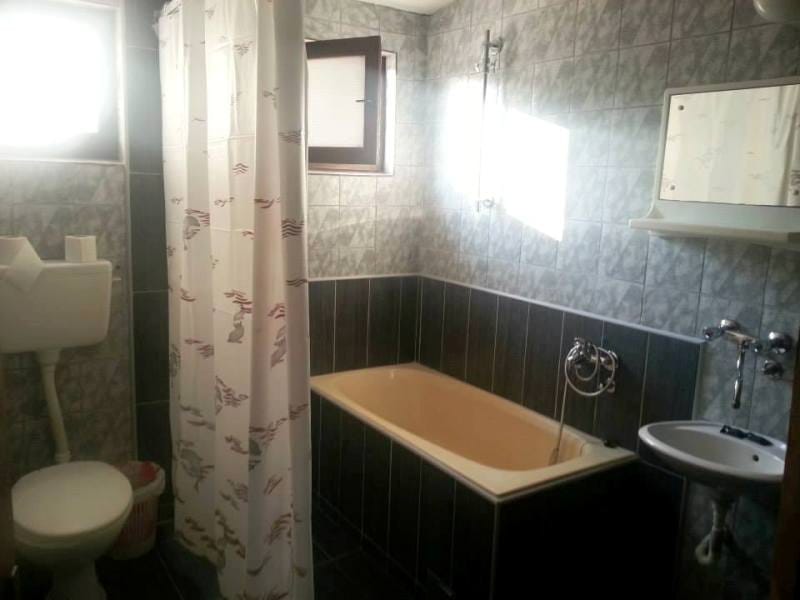 Kupatilo u kući u Sutomoru, Crna Gora: pločice u sivim tonovima, kada, lavabo i toalet, prozor za ventilaciju.