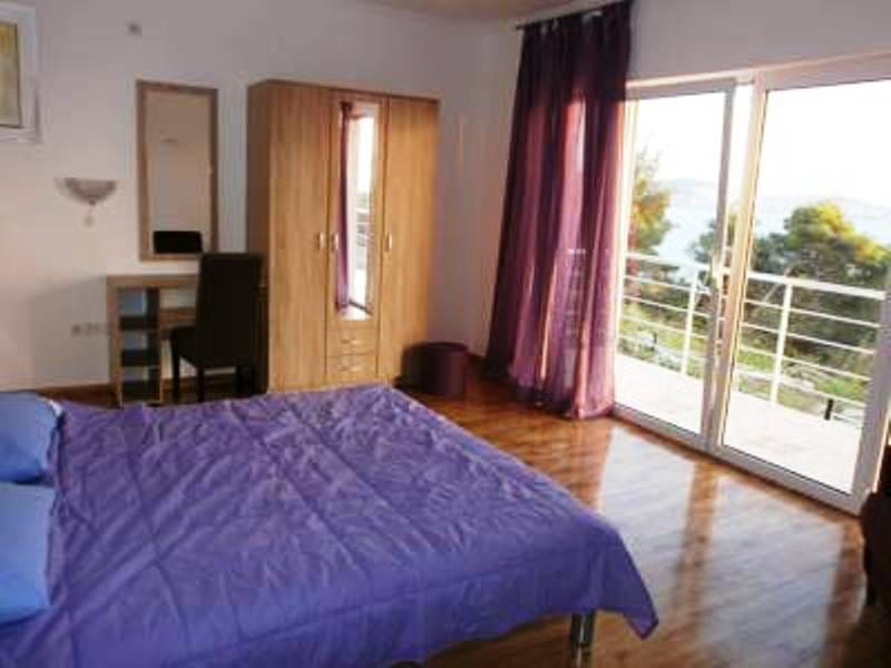 Spavaća soba u hotelu Šušanj, Crna Gora: bračni krevet, drveni ormar, toaletni sto i pogled na more sa balkona.