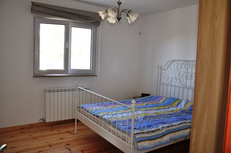 Svetla spavaća soba sa kovanim krevetom i drvenim podom u kući na poluostrvu Luštica, Crna Gora.