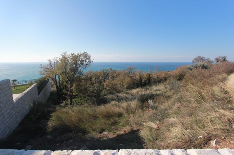 Grundstück in Reževići, Montenegro: Panoramablick auf das Meer und die Hügel mit Steinmauer auf dem Gelände.