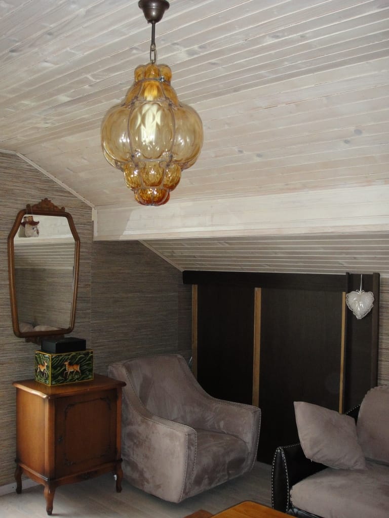 Intérieur du salon dans un appartement à Radovici, Monténégro : fauteuil moelleux, meuble vintage avec miroir et lustre ambré.