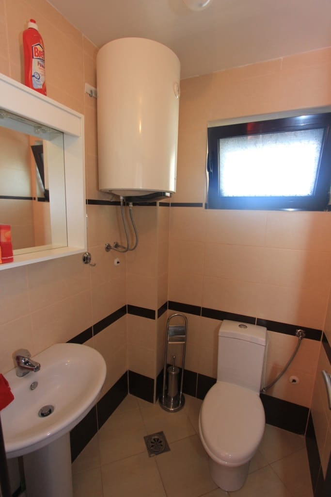 Kupatilo u stanu, Rafailovići, Crna Gora: bež pločice, bojler, lavabo, toalet i prozor.
