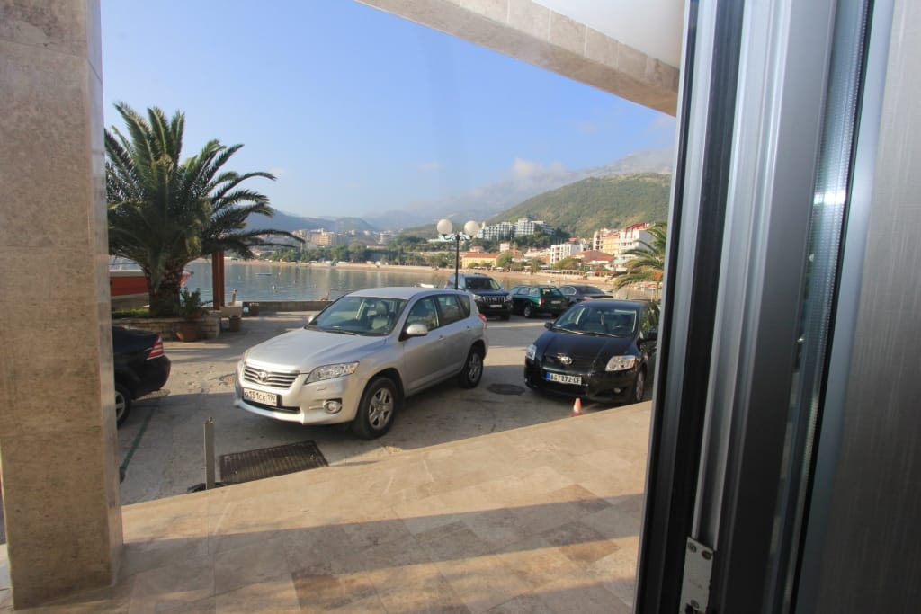 Pogled sa terase poslovnog prostora u Rafailovićima, Crna Gora: parking pored mora, palme i planinski pejzaž.