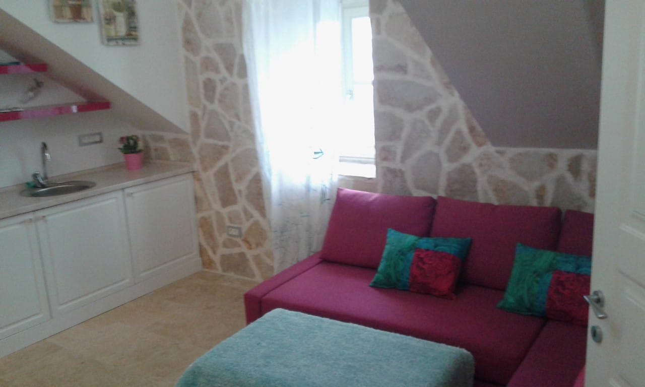 Wohnzimmer mit Küche und Steinverkleidung der Wände in einer Villa in Perast, Montenegro: rotes Sofa und helles Interieur.
