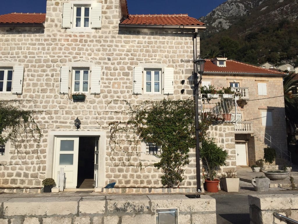 Traditionelle Steinvilla in Perast, Montenegro: helle Steinfassade, weiße Fensterläden und Bergblick.