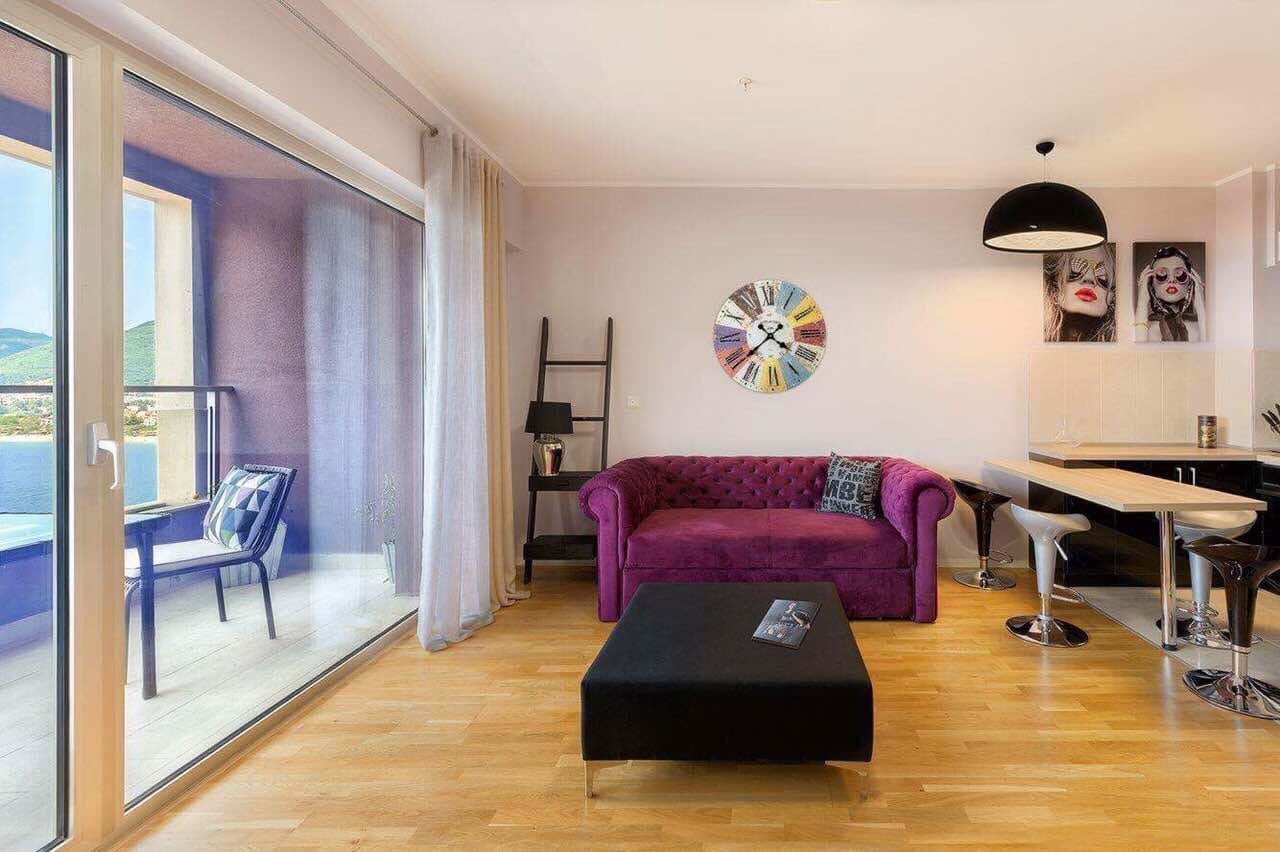 Dnevna soba sa ljubičastom sofom i panoramskim pogledom na more u stanu, Bečići, Crna Gora.