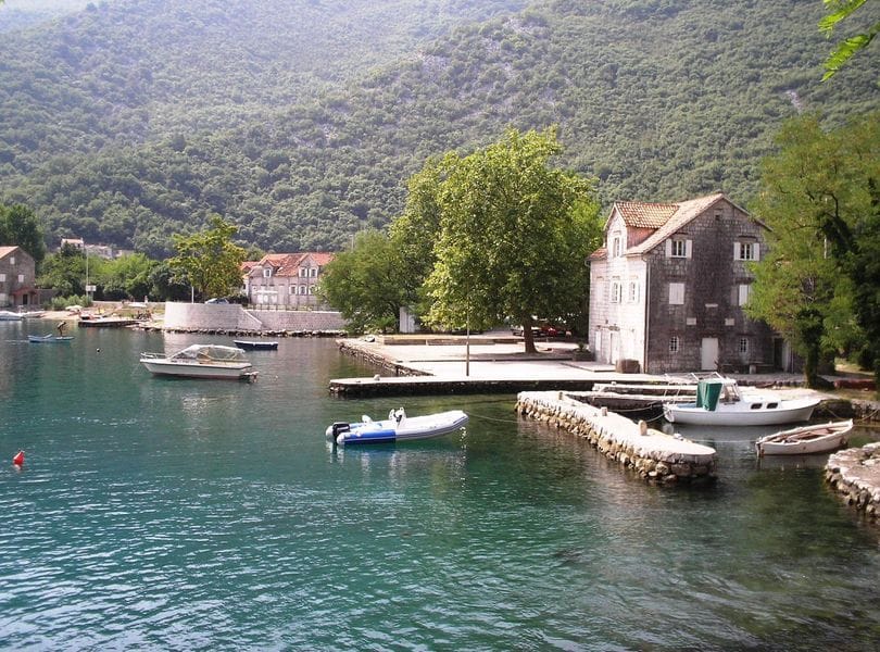 Pogled na kamenu kuću i pristanište s čamcima u naselju Morinj, Crna Gora, slikovit pejzaž uz Bokokotorski zaliv.
