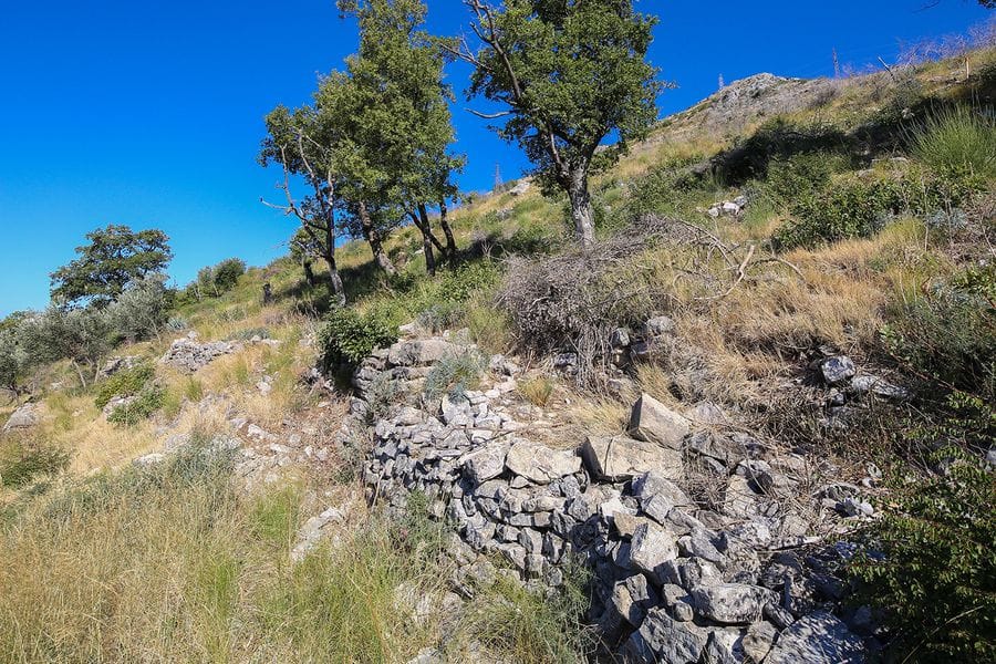 Građevinsko zemljište u Reževićima, Crna Gora: brdovit teren sa kamenim zidom, drvećem i panoramskim pogledom.