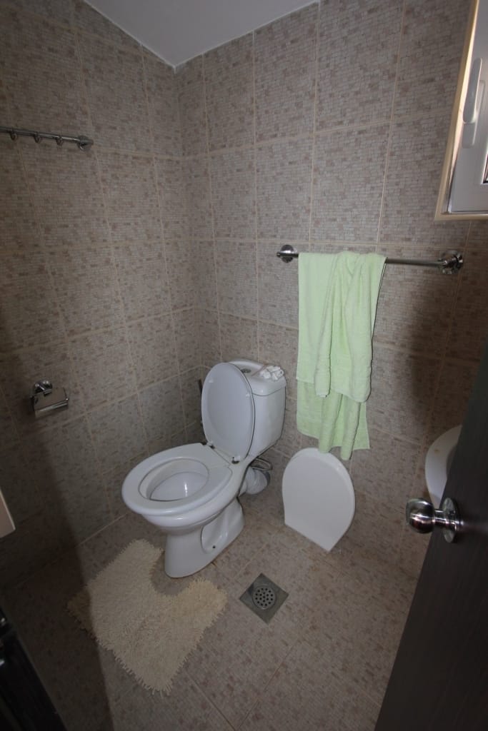 Kupatilo sa belom sanitarnom opremom i bež pločicama u kući na Barskoj rivijeri, Crna Gora.