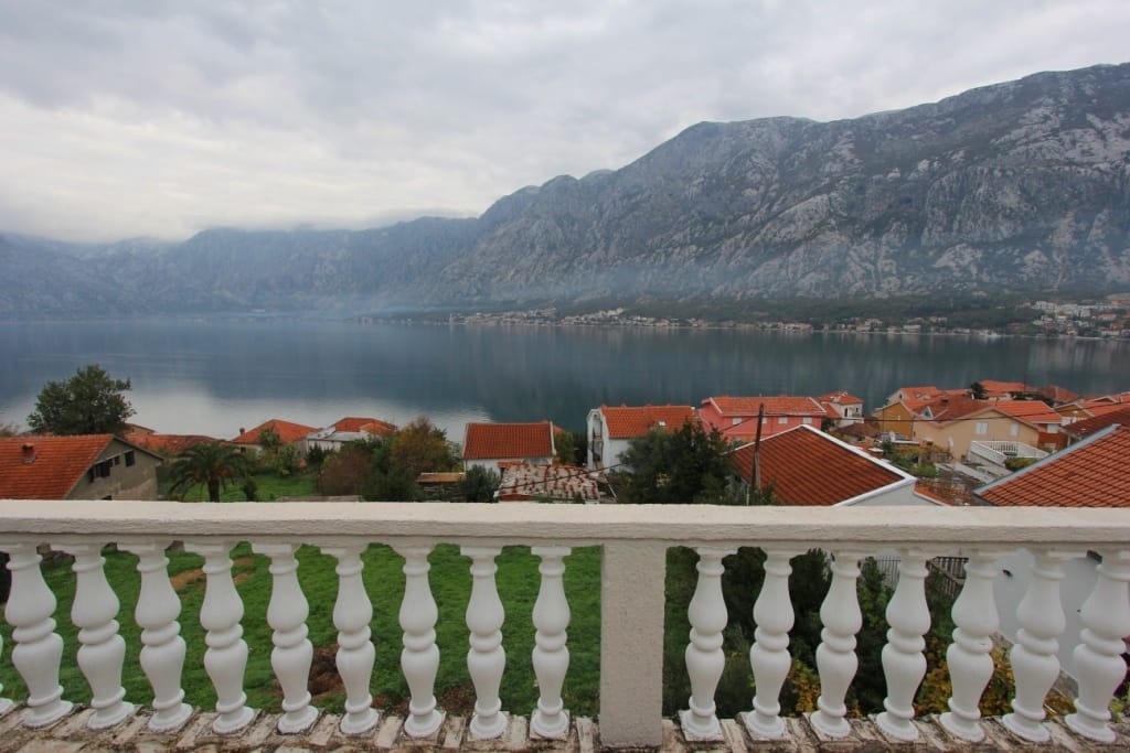 Widok z balkonu z białą balustradą na Zatokę Kotorską i góry w Prčanj, Czarnogóra: panorama morza i dachów z dachówki.