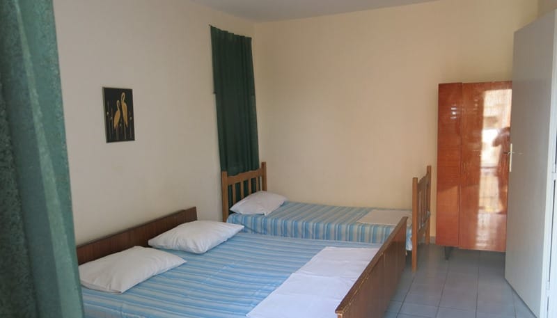 Spavaća soba sa dva kreveta i drvenim ormarom u mini-hotelu, Rafailovići, Crna Gora. Svetla završna obrada i pod od pločica.