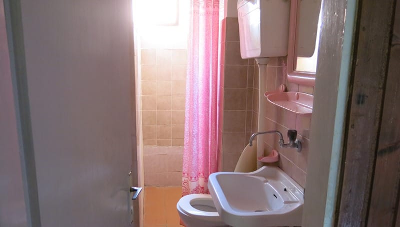 Kupatilo u mini-hotelu, Rafailovići, Crna Gora: bela sanitarija, roze zavesa i zidovi obloženi pločicama.