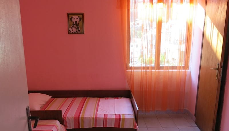 Spavaća soba u mini-hotelu Rafailovići, Crna Gora: jednokrevetni kreveti, roze zidovi i prozor sa narandžastim zavesama.