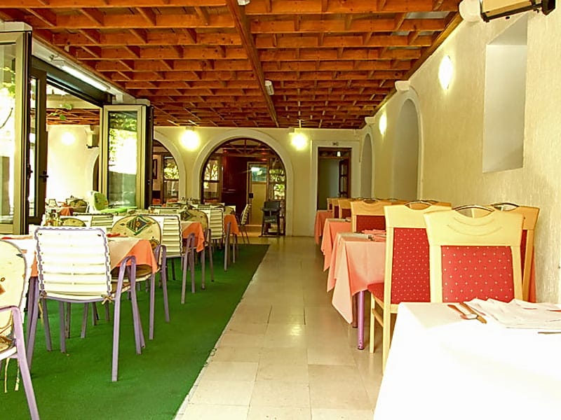 Wnętrze restauracji hotelowej w Petrovacu, Czarnogóra: zadaszony taras z drewnianym sufitem, stoliki i krzesła dla gości.