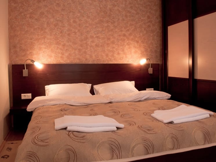 Przytulna sypialnia z łóżkiem dwuosobowym w hotelu Petrovac, Czarnogóra: ciemne meble, kinkiety i dekoracje.