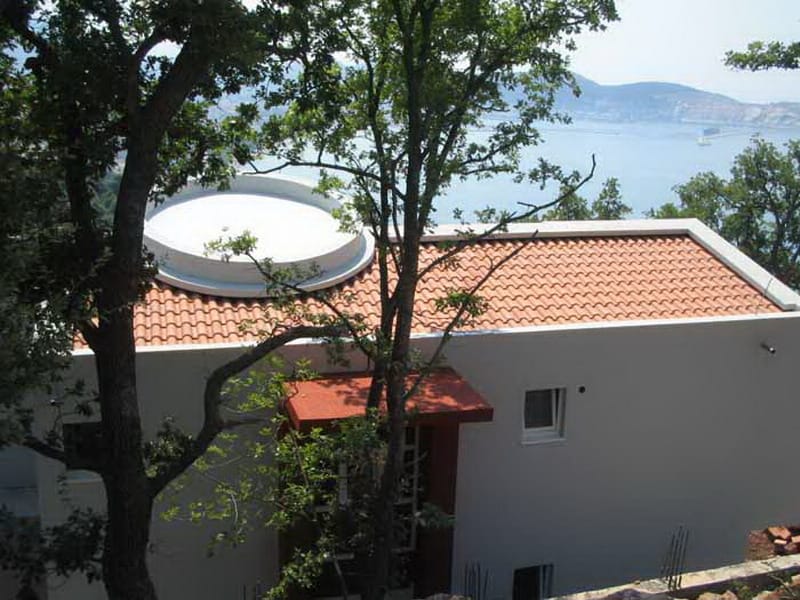 Savremena kuća sa krovom od crepa i pogledom na more u Šušnju, Crna Gora, okružena zelenilom i drvećem.