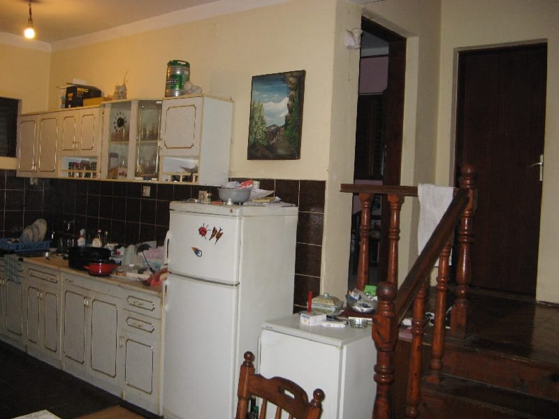 Kuhinja u kući u Šušnju, Crna Gora: svetao kuhinjski nameštaj, tamni zidni panel, frižider i drveno stepenište na drugi sprat.