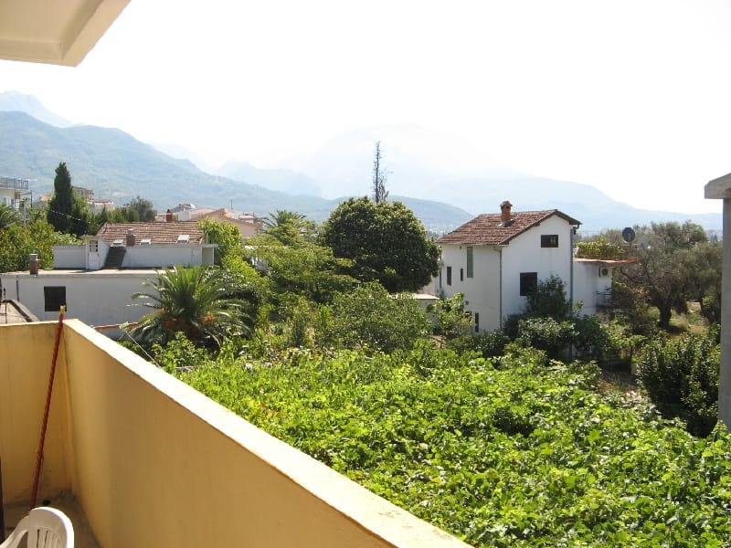 Pogled sa balkona kuće u Šušnju, Crna Gora: zelena bašta, prijatne vile i slikoviti planinski pejzaži u pozadini.