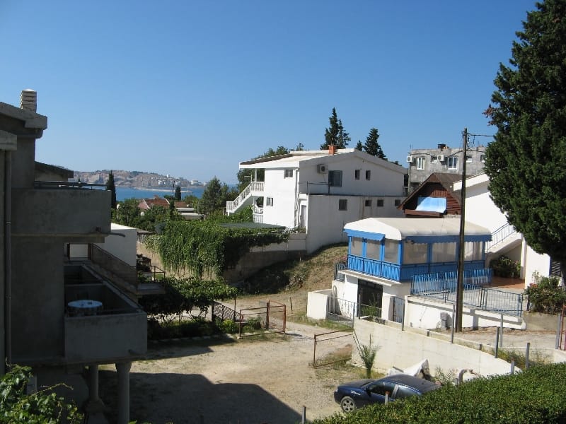 Pogled na privatne kuće i morski zaliv u naselju Šušanj, Crna Gora, sa dvorištem i parkingom.