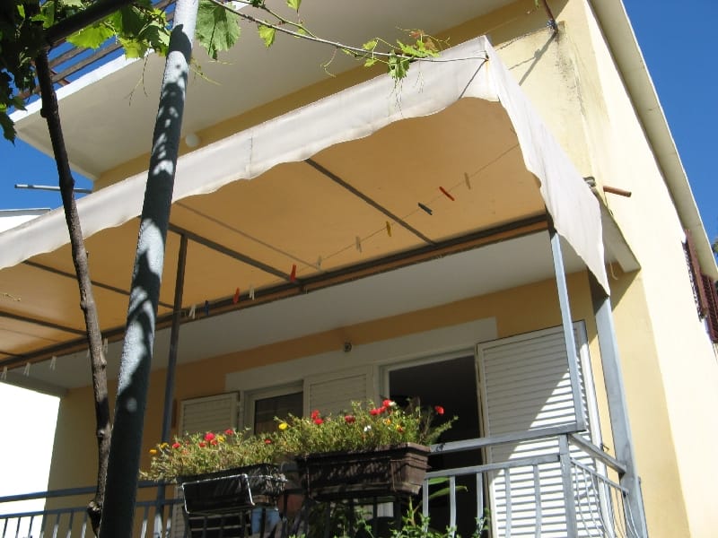Balkon kuće u Šušnju, Crna Gora: nadstrešnica od sunca, konopac za veš i saksije sa cvećem na metalnoj ogradi.