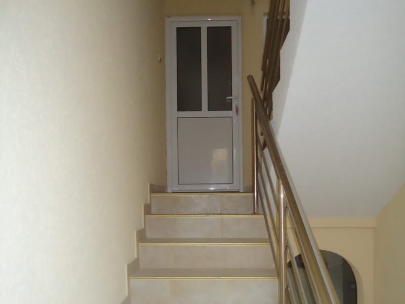 Stepenište sa metalnim ogradama i svetlom završnom obradom u kući u Šušnju, Crna Gora. Ulazna vrata u apartman.