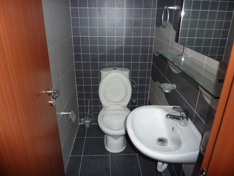 Savremeno kupatilo sa tamnim pločicama, umivaonikom i toaletom u stanu u gradu Tivat, Crna Gora.