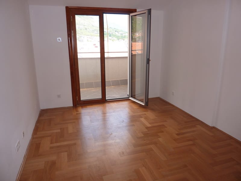 Svetao dnevni boravak sa parketom i izlazom na balkon u stanu, grad Tivat, Crna Gora.