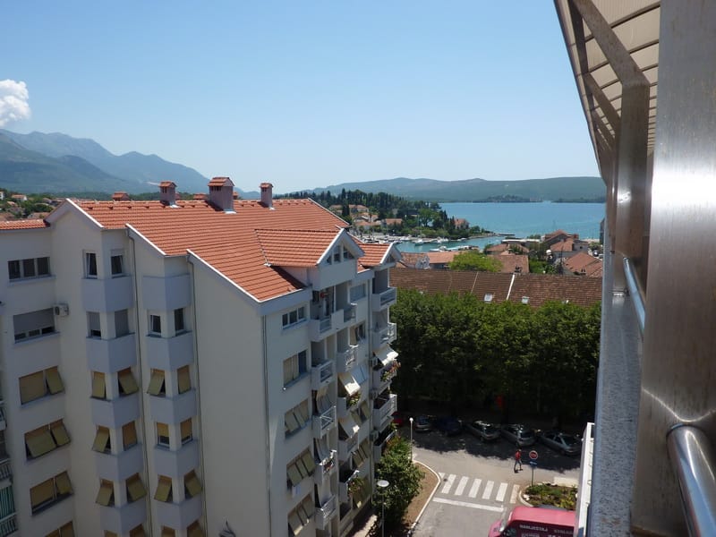 Pogled sa balkona stana u Tivtu, Crna Gora: panorama mora, planina i stambenog naselja sa krovovima od crepa.