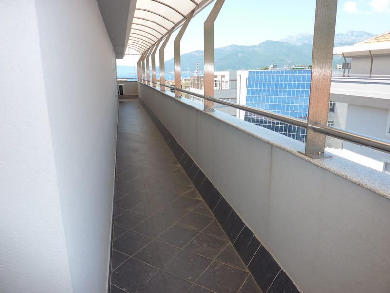 Dugačak balkon sa nadstrešnicom i pogledom na planine i more u stanu, grad Tivat, Crna Gora. Porcelanski pločice na podu.