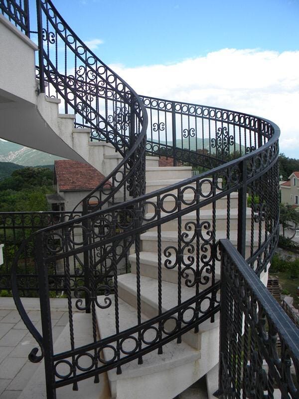 Kręcone schody z kutą balustradą w willi w Herceg Novi, Czarnogóra, z panoramicznym widokiem na góry i miasto.