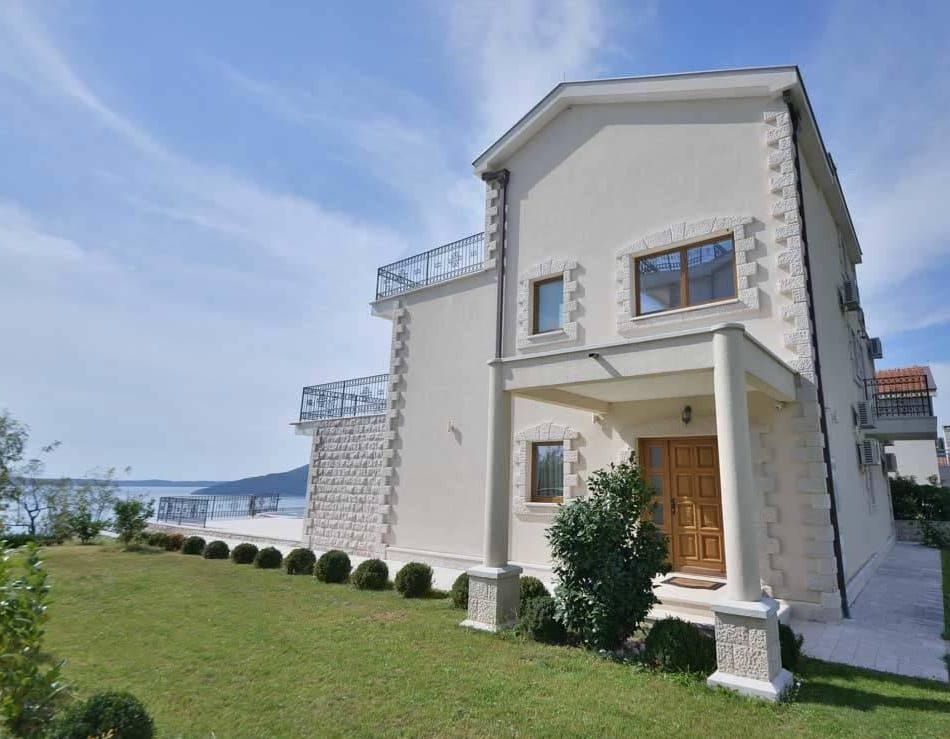 Dwupiętrowa willa z tarasami i widokiem na morze w Herceg Novi, Czarnogóra: kamienna fasada i zadbany ogród.
