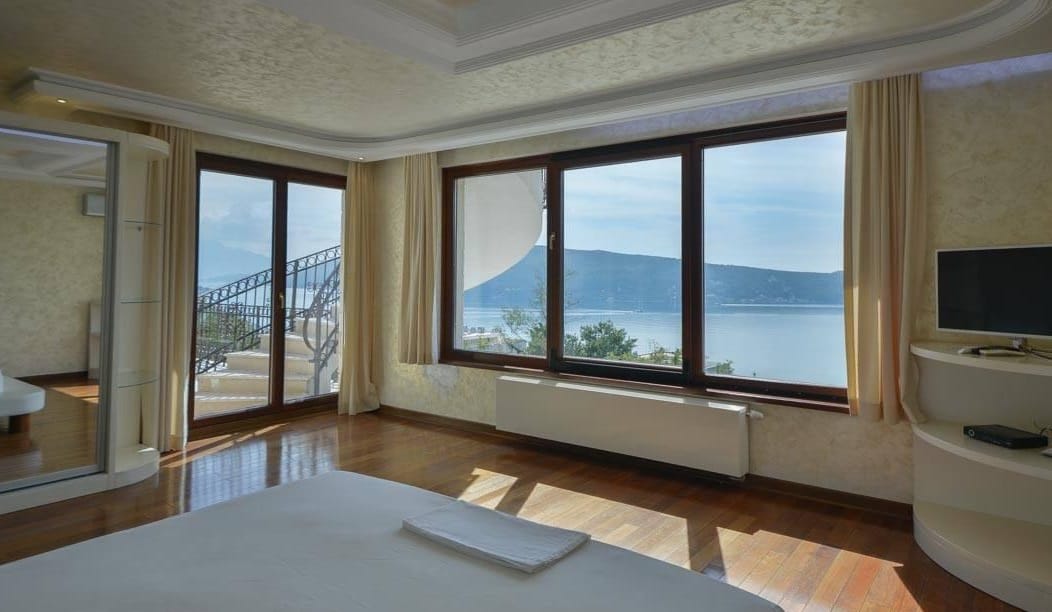 Sypialnia w willi w Herceg Novi, Czarnogóra: panoramiczne okna z widokiem na morze, parkiet i wyjście na taras.