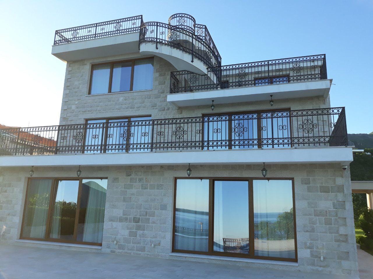 Trzypiętrowa kamienna willa w Herceg Novi, Czarnogóra, z panoramicznymi oknami, tarasami i kutymi balustradami.